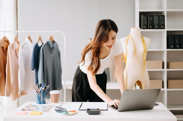 Mulher alfaiate asiática trabalhando em roupas em atelier de alfaiate bela jovem designer de moda sorriso e após o sucesso em estúdio moderno