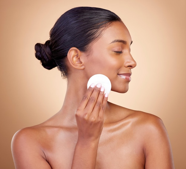 Mulher almofada de algodão e cuidados com a pele de cosméticos faciais para bem-estar estético em fundo de estúdio Modelo feminino indiano feliz beleza limpa e produto de dermatologia facial para remoção de maquiagem brilho e brilho