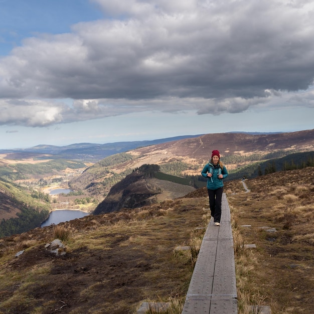 Mulher alpinista andando em um caminho de madeira no parque nacional de Glendalough, montanhas de wicklow, irlanda