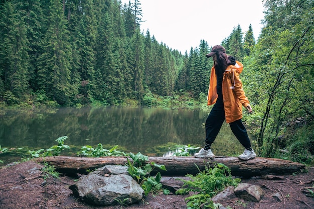 Mulher alpinista com mochila e capa de chuva amarela olhando para o espaço da cópia do lago da montanha