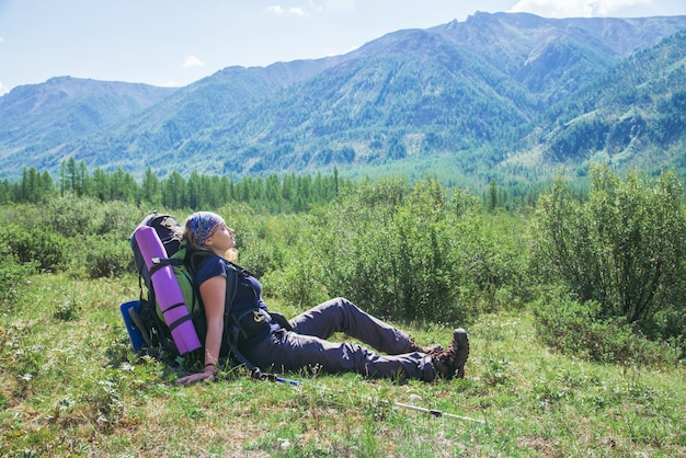 Mulher alpinista com mochila sentado na grama verde e sinta-se relaxar com os olhos fechados