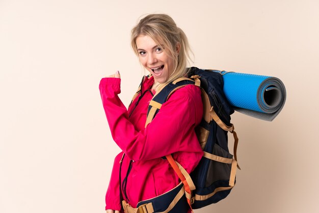 Mulher alpinista com uma grande mochila sobre um fundo isolado comemorando uma vitória