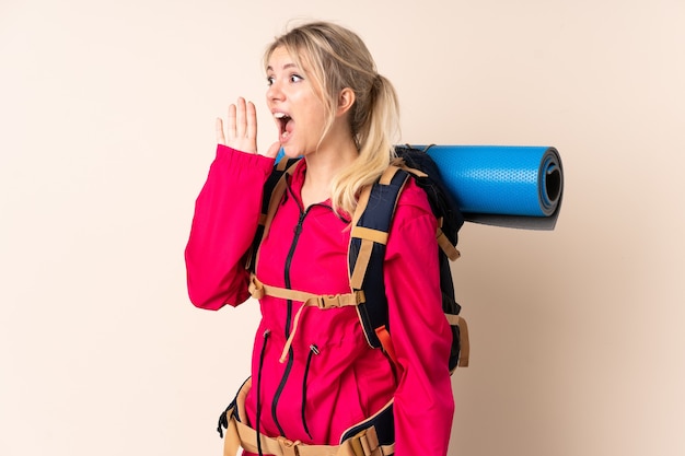 Mulher alpinista com uma mochila grande sobre um fundo isolado gritando com a boca bem aberta