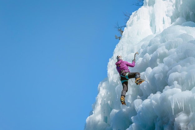 Foto mulher alpinista escalando uma cachoeira congelada