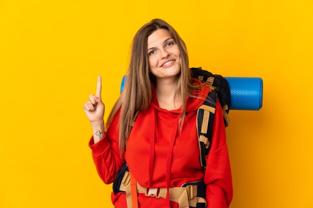 Mulher alpinista eslovaca com uma grande mochila isolada em um fundo amarelo mostrando e levantando um dedo em sinal dos melhores