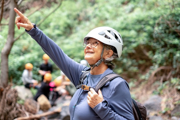 Mulher alpinista sênior com mochila e capacete aproveitando o dia de trekking na montanha Turista ativo