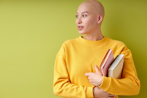 Mulher americana careca olhando para a câmera segurando livros nas mãos, alopecia e câncer