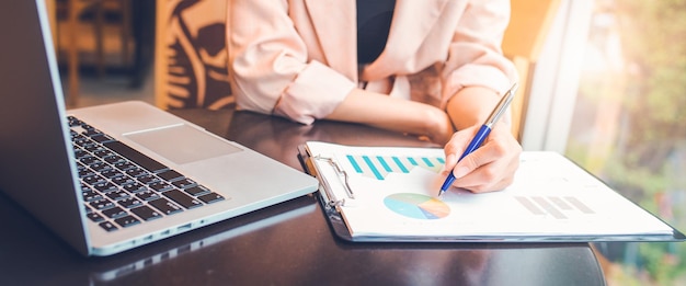 Mulher analisando o gráfico de dados da situação do estoque ela usa uma caneta e um laptop para banner da web