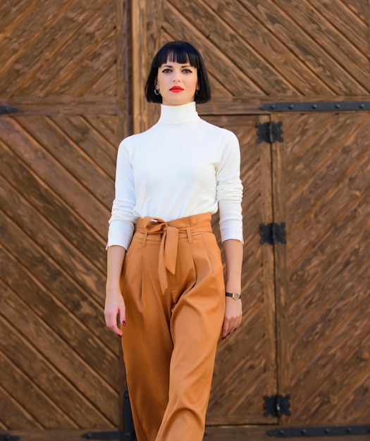 Mulher anda com confiança Mulher morena elegante fica ao ar livre fundo de madeira Conceito de moda e estilo Menina com maquiagem posando em roupas da moda Roupa elegante senhora alta e magra