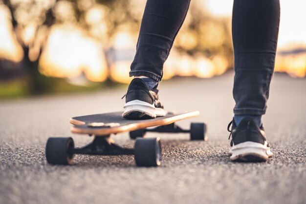 Mulher anda na estrada reta no longboard na hora do pôr do sol Skatista em roupas casuais treinando a bordo durante o pôr do sol da noite com luz laranja Garota segura o longboard nas mãos