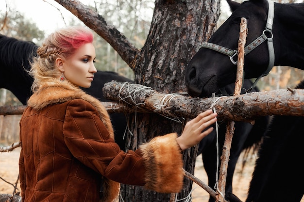 Mulher andando com cavalo outono na natureza. Rosto de menina maquiagem rosa quente criativa, coloração de cabelo. Retrato de uma menina com um cavalo. Passeios a cavalo na floresta de outono. Roupas de outono e maquiagem vermelha brilhante