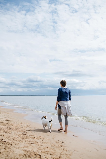 Mulher andando com seu cachorro na praia Vista traseira