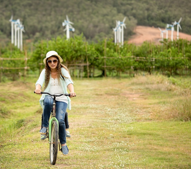 Mulher andando de bicicleta em campo com turbinas eólicas no fundo