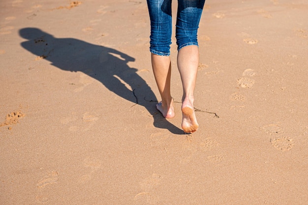 Mulher andando descalça na praia durante um dia ensolarado vista traseira fechada