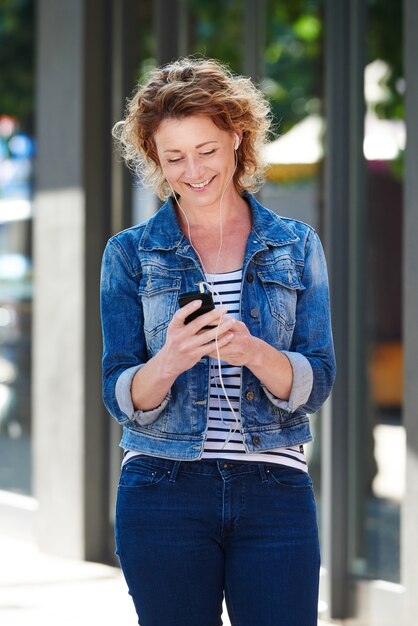 Mulher andando e sorrindo na cidade com celular