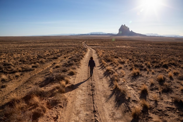 Mulher andando em uma estrada de terra no deserto seco com um pico de montanha ao fundo