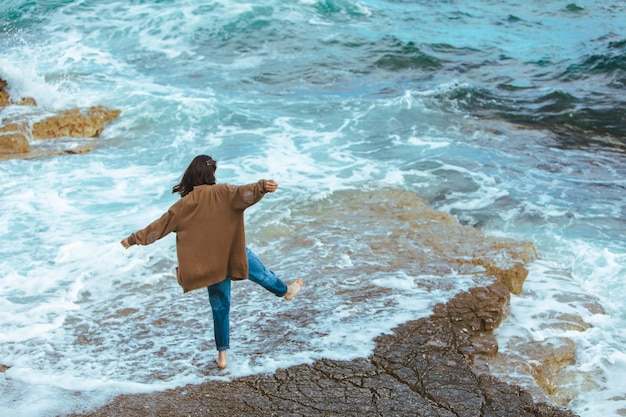 Mulher andando pela praia rochosa em jeans molhados com os pés descalços férias no mar