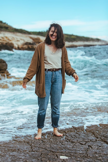 Mulher andando pela praia rochosa em jeans molhados com os pés descalços