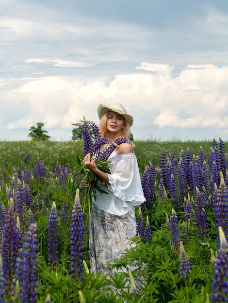 Mulher andando por um prado florescente segurando um buquê de lupinos aproveitando o silêncio da natureza e