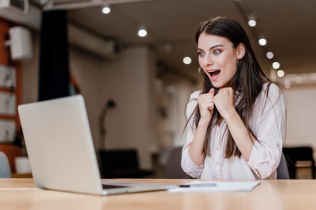 Mulher animada e surpresa com laptop no escritório