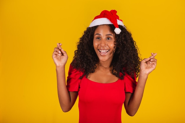 Mulher animada expressiva com chapéu de Papai Noel em fundo amarelo.