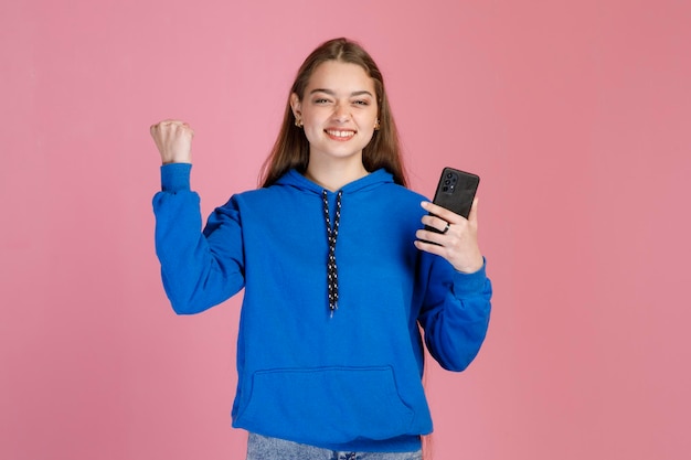 Mulher animada feliz com smartphone levantando punho tenso mostrando gesto vencedor no estúdio