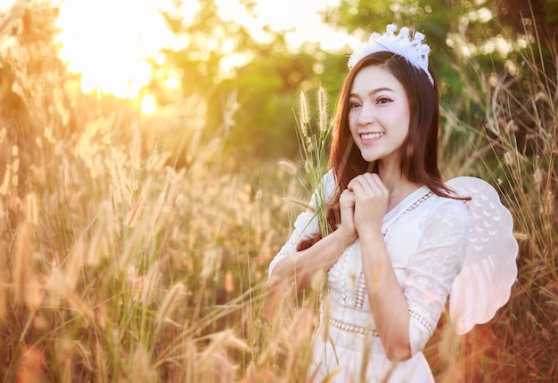 Mulher anjo em um campo de grama com luz solar