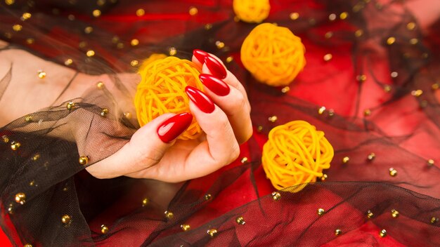 Mulher anônima com manicure vermelha com bolas de vime decorativas em fundo vermelho
