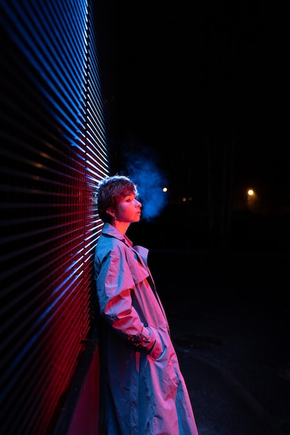 Mulher ansiosa e abandonada em luz neon inclinada perto da parede enquanto fica na rua à noite fria