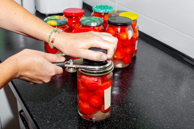 mulher aperta as tampas de um frasco de tomates picados vermelhos com uma costura Conservação de vegetais
