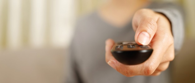 Mulher aperta o controle remoto da TV online em casa