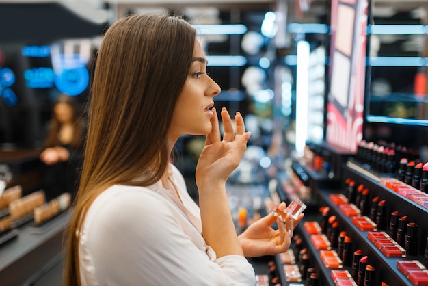 Mulher aplica batom em loja de cosméticos. comprador em vitrine em salão de beleza de luxo, cliente mulher no mercado de moda