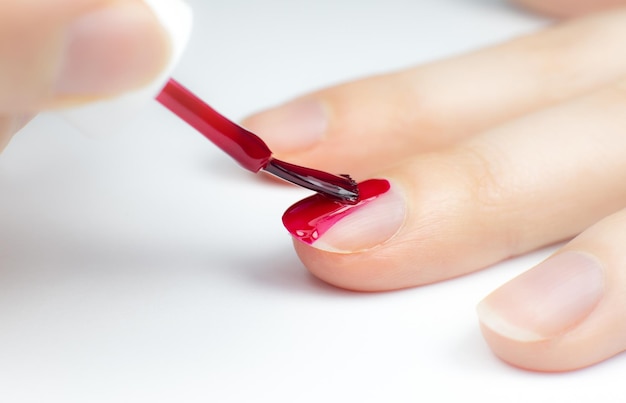 Mulher aplica esmalte vermelho xAGirl fazendo manicure Procedimentos de salão em casa Mãos e unhas bonitas Fechar foto macro