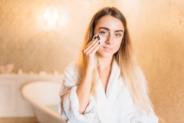 Mulher aplicando creme cosmético facial, cuidados com a pele no banheiro. Cuidados com o corpo e higiene, saúde, produtos de beleza