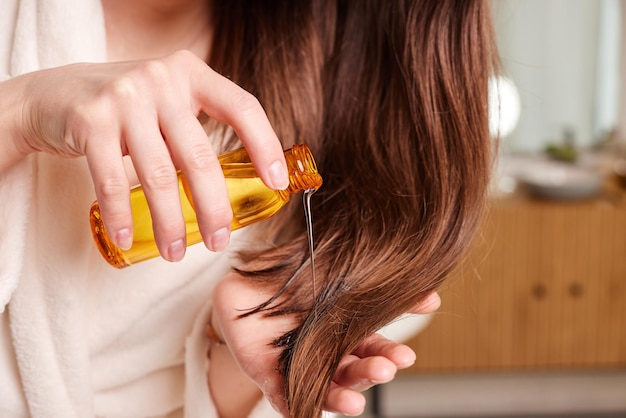 Mulher aplicando óleo para o cabelo no conceito moderno de cuidados com o cabelo no banheiro