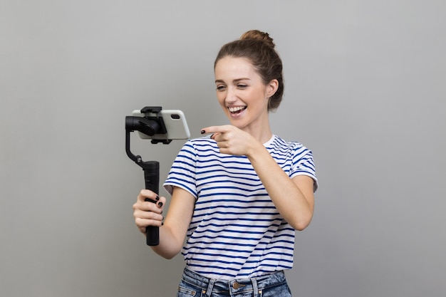 Mulher apontando para câmera de celular com sorriso fluindo conversando com seguidores usa steadicam