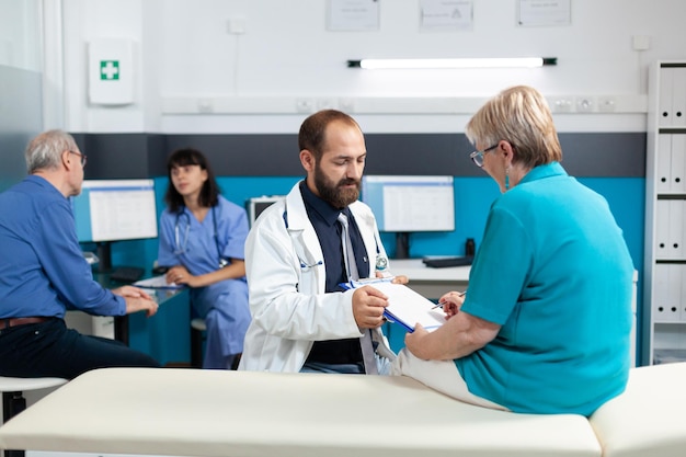 Mulher aposentada, assinando documentos de verificação e conversando com o médico para tratamento. Médico pedindo ao paciente a assinatura em papéis, para tratar lesões ortopédicas com recuperação quiroprática.