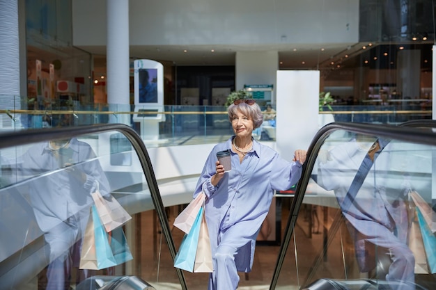 Mulher aposentada feliz a andar de escada rolante num centro comercial