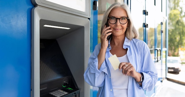 Foto mulher aposentada retira dinheiro de um caixa eletrônico na rua