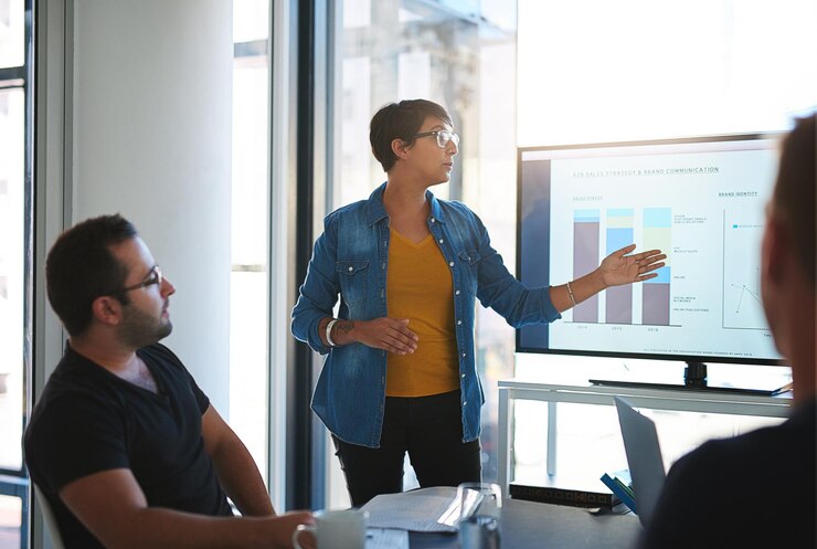 Foto mulher apresentação e gráficos no ecrã escritório e grupo com revisão estratégia b2b pessoas de negócios orador e informação com apontando feedback e quadro para gráficos para comunicação de marca
