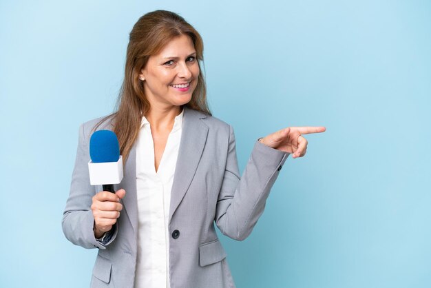 Mulher apresentadora de TV de meia-idade sobre fundo azul isolado, apontando o dedo para o lado