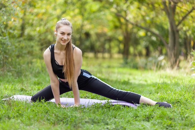 Mulher apta ativa em roupas esportivas está praticando exercícios de alongamento no parque em um dia ensolarado brilhante conceito de fitness de estilo de vida saudável