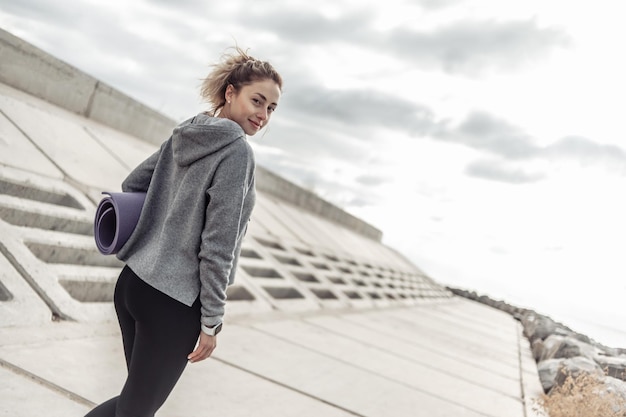 Mulher apta em roupas esportivas com tapete ao ar livre Estilo de vida saudável