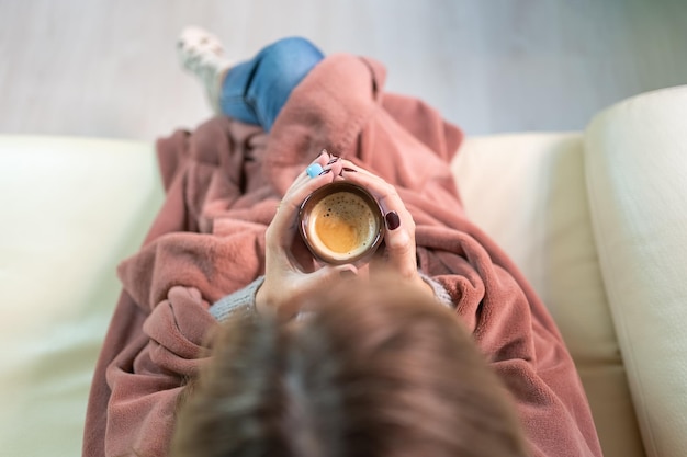 Mulher aquecendo as mãos com uma xícara de café quente enquanto aproveita o calor de casa no meio do inverno