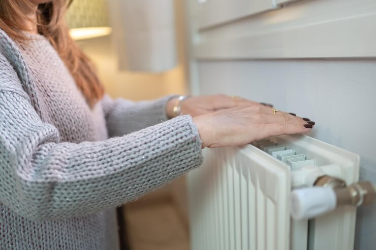 Mulher aquecendo as mãos em um radiador por causa do frio do inverno