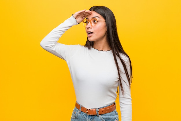 Mulher árabe bonita nova contra o amarelo longe mantendo a mão na testa.