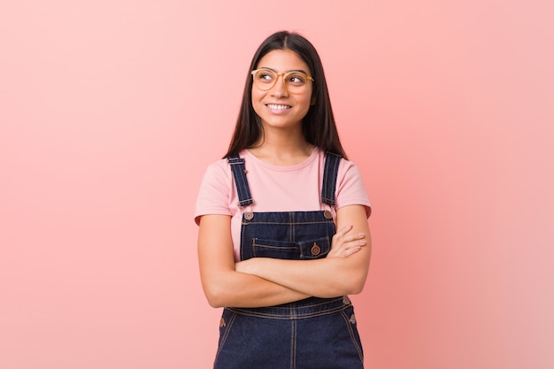 Mulher árabe bonita nova que veste um sorriso do dungaree das calças de brim seguro com braços cruzados.