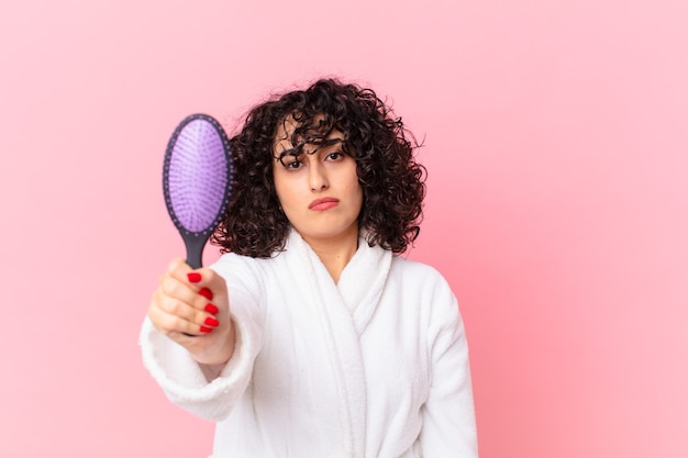 Mulher árabe bonita usando roupão de banho e segurando uma escova de cabelo