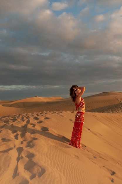 Mulher árabe dançando dança do ventre nas dunas do deserto ao pôr do sol