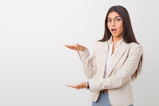 Mulher árabe do negócio novo isolada contra um branco chocado e surpreendido guardando um copyspace entre as mãos.